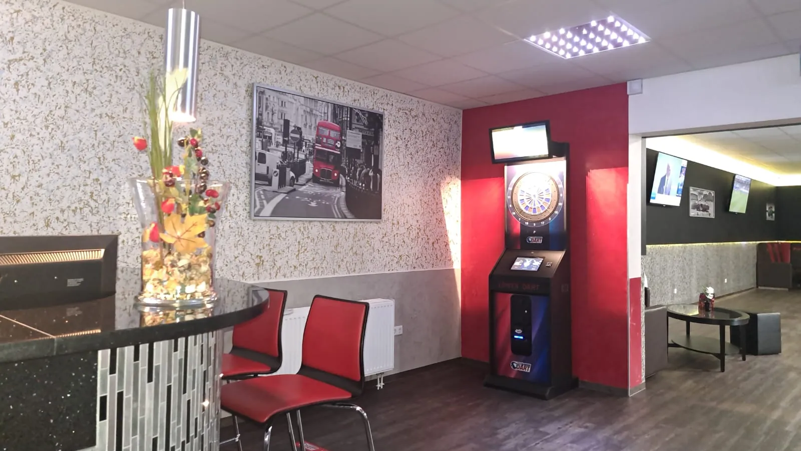 E-Dart-Automat mit Monitor an einer roten Wandsäule bei Billard Wesel, davor rote Stühle, an der Wand ein London-Bild mit rotem Doppeldeckerbus